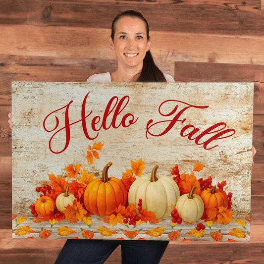 Woman holding Hello Fall Canvas wall art with pumpkins and autumn leaves design against wooden background